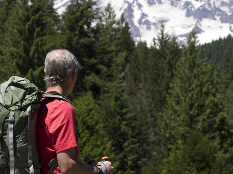 A man with a backpack standing on a trail looking towards Mount Rainier